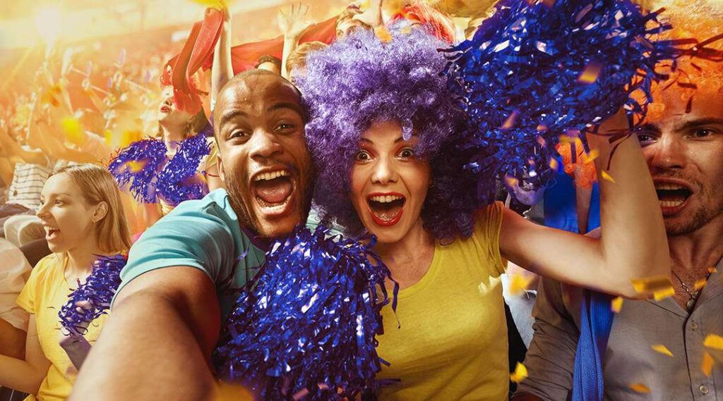 Group of fans cheering at a packed stadium, holding pom-poms and celebrating during a live sporting event